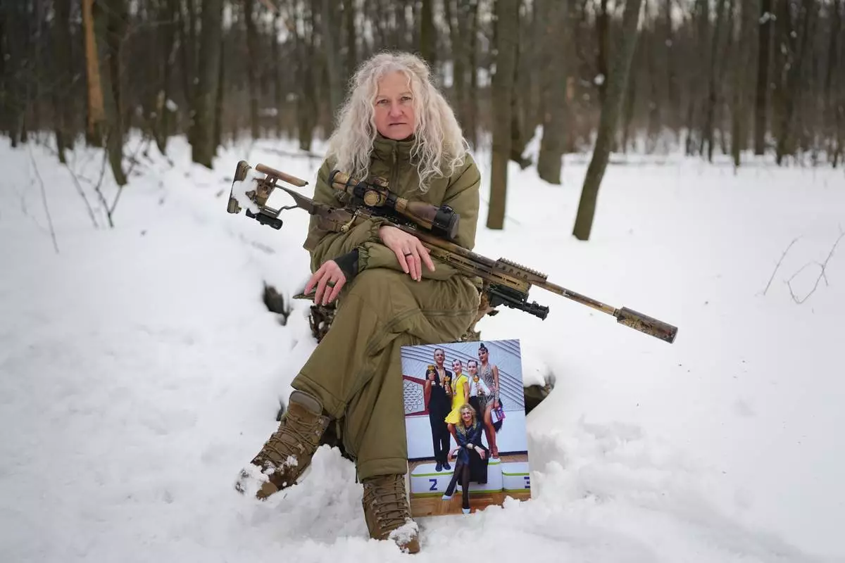 Tetiana Khimion 47, now a sniper in the Ukrainian army, poses with a photograph of herself as a dance teacher taken before Russia's full-scale invasion, in a park in Kyiv, Ukraine, Sunday, Feb. 22, 2026. (AP Photo/Sergei Grits)