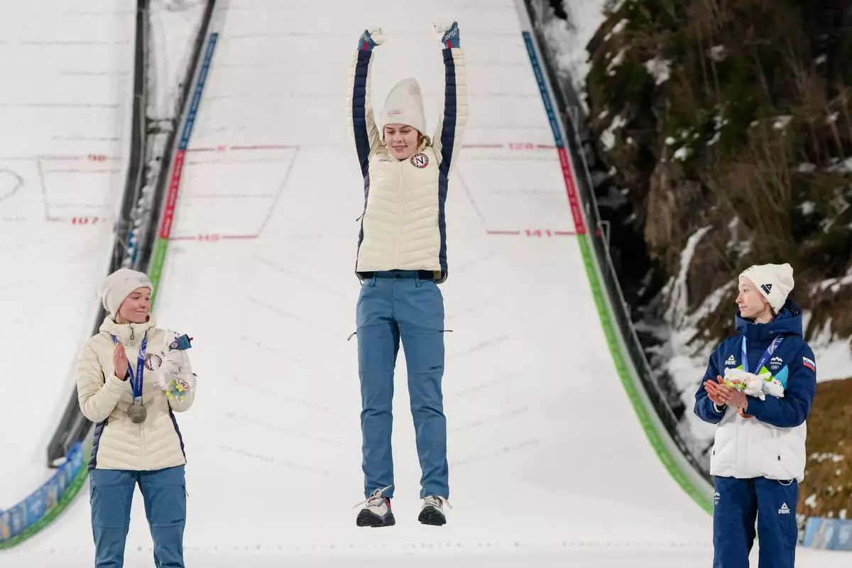 Gold medalist Anna Odine Stroem, of Norway, celebrates on the podium flanked by silver medalist Eirin Maria Kvandal, also of Norway, and bronze medalist Nika Prevc, of Slovenia, right, after the ski jumping women's large hill individual at the 2026 Winter Olympics, in Predazzo, Italy, Sunday, Feb. 15, 2026. (AP Photo/Kirsty Wigglesworth)