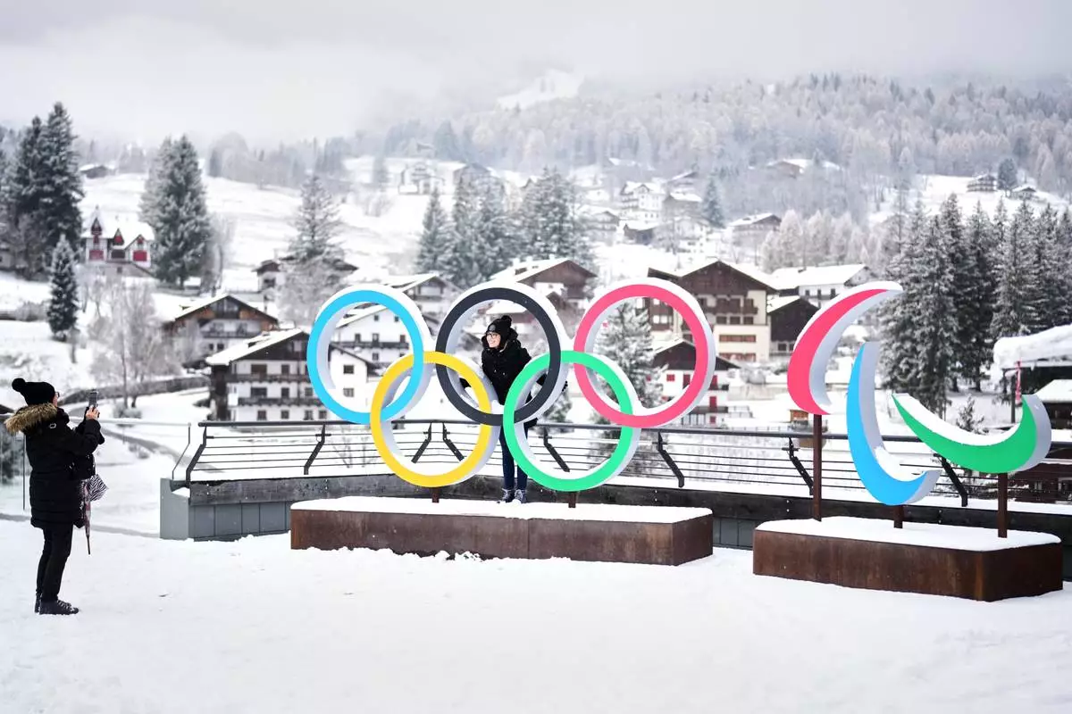 FILE - People take photos in front of the Milan Cortina Winter Olympics and Paralympics rings, in Cortina D'Ampezzo, Nov. 20, 2025. (AP Photo/Andrew Medichini, File)