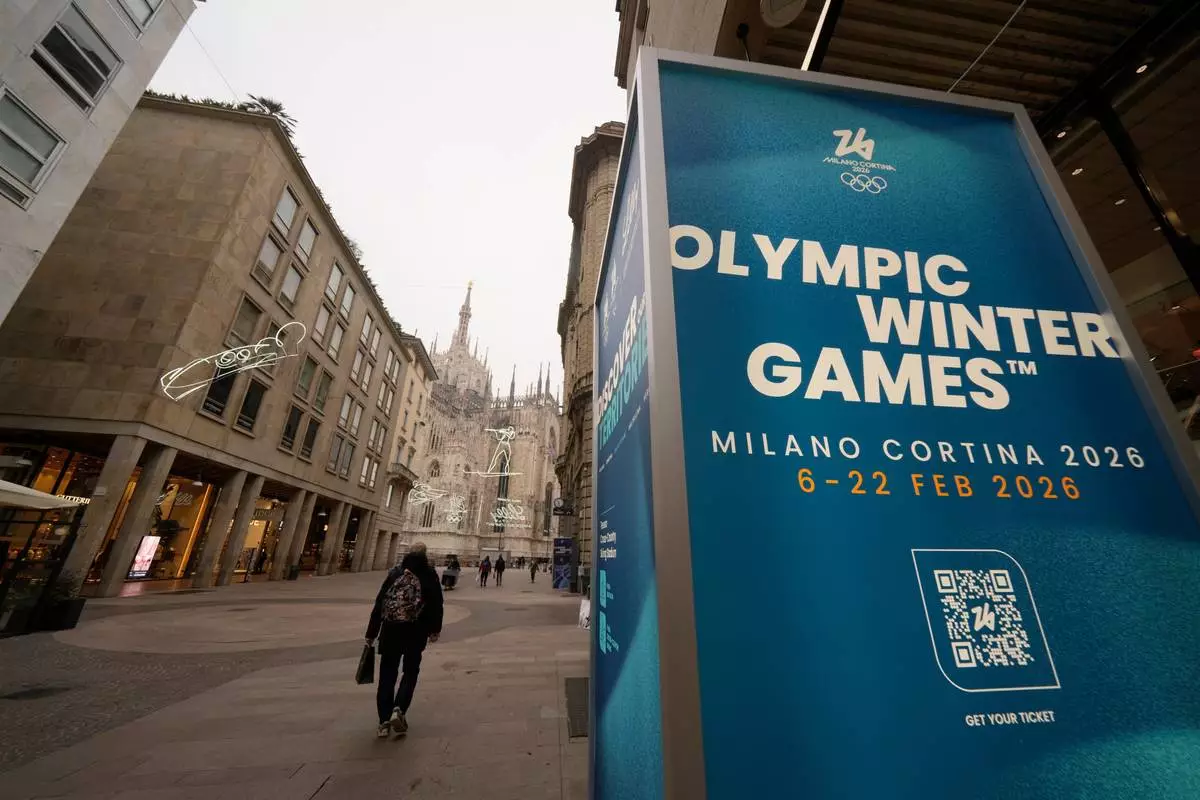 FILE - People walk along the Corso Vittorio Emanuele II, the main downtown street, near a sign for the upcoming Milan-Cortina Winter Olympics in Milan, Italy, Jan. 9, 2026. (AP Photo/Luca Bruno, File)