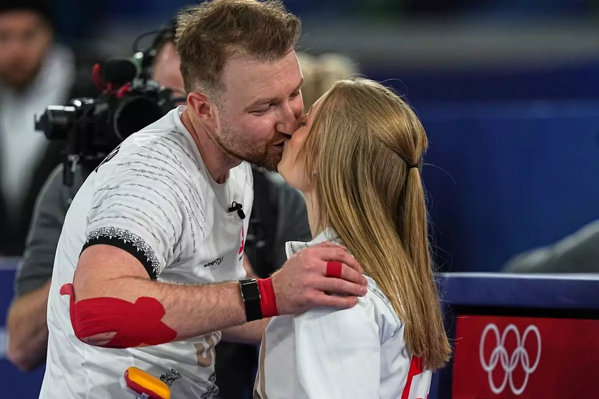 Switzerland's Yannick Schwaller and Briar Schwaller-Huerlimann kiss during the mixed doubles round robin phase of the curling competition against Britain, at the 2026 Winter Olympics, in Cortina d'Ampezzo, Italy, Sunday, Feb. 8, 2026. (AP Photo/Fatima Shbair)