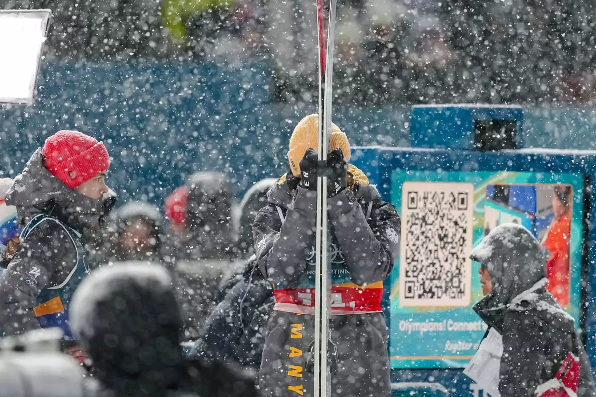 Andreas Wellinger, center, and Philipp Raimund, of Germany, left, react as a snowfall interrupts the final round jump of the ski jumping men's super team competition at the 2026 Winter Olympics, in Predazzo, Italy, Monday, Feb. 16, 2026. (AP Photo/Matthias Schrader)