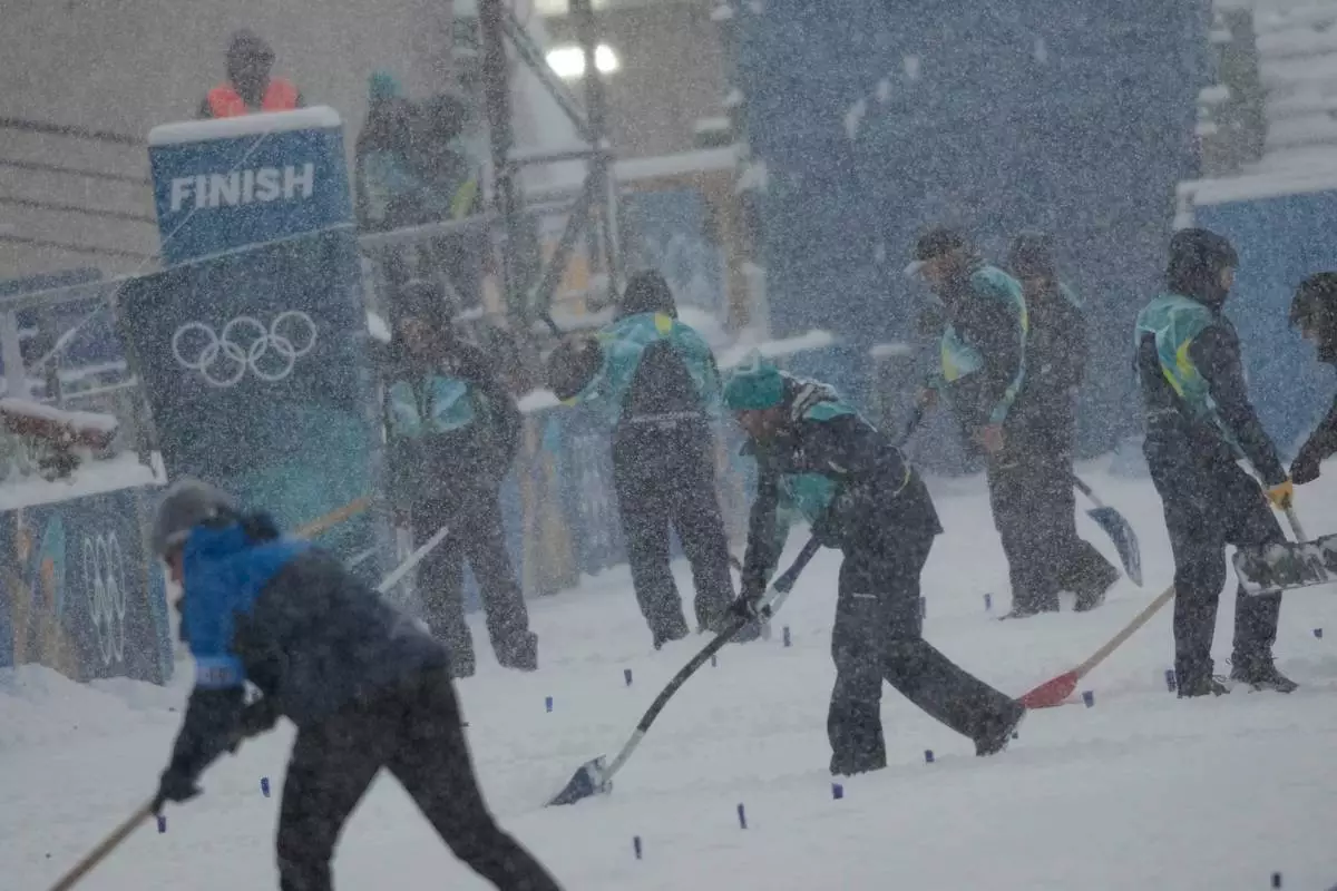 Volunteers remove snow on the finish area before the Biathlon Men's 4 x 7.5km Relay at the 2026 Winter Olympics, in Anterselva, Italy, Tuesday, Feb. 17, 2026. (AP Photo/Christophe Ena)