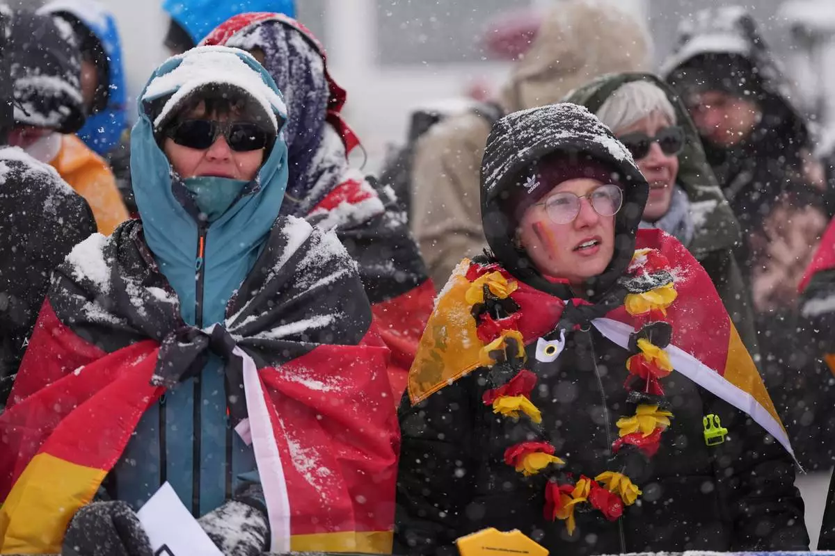 Fans for Germany's Emma Weiss brave heavy snow during a weather delay before the women's freestyle skiing aerials qualifications at the 2026 Winter Olympics, in Livigno, Italy, Tuesday, Feb. 17, 2026. (AP Photo/Gregory Bull)
