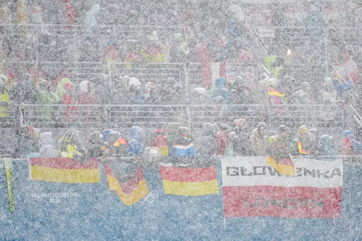 Germany and Poland fans on the stands wait while a snowfall interrupts the final round jump of the ski jumping men's super team competition at the 2026 Winter Olympics, in Predazzo, Italy, Monday, Feb. 16, 2026. (AP Photo/Matthias Schrader)