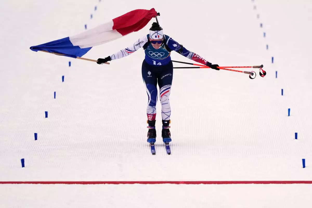 Julia Simon, of France, skis with her country's flag as she crosses the finish line for gold in the women's 4x6-kilometer relay biathlon race at the 2026 Winter Olympics in Anterselva, Italy, Wednesday, Feb. 18, 2026. (AP Photo/Mosa'ab Elshamy)