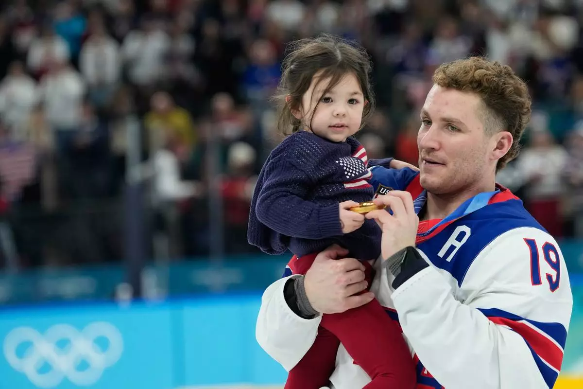 ADDS NAME OF CHILD United States' Matthew Tkachuk (19) carries Noa Gaudreau, following a men's ice hockey gold medal game between Canada and the United States at the 2026 Winter Olympics, in Milan, Italy, Sunday, Feb. 22, 2026. (AP Photo/Petr David Josek)