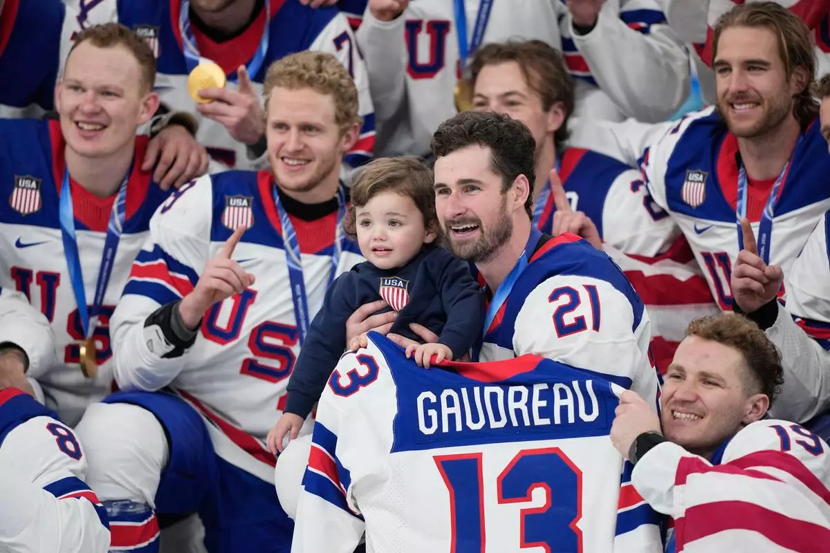 United States' Dylan Larkin (21) holds Johnny, the son of the late playe Johnny Gaudreau while posing with teammates after a men's ice hockey gold medal game between Canada and the United States at the 2026 Winter Olympics, in Milan, Italy, Sunday, Feb. 22, 2026. (AP Photo/Petr David Josek)