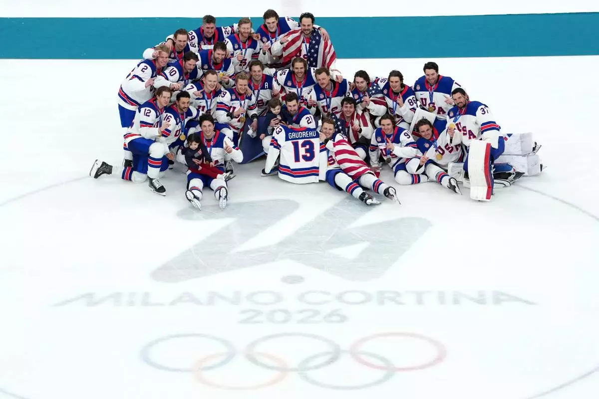 ADDS ID FOR CHILDREN United States players pose for pictures with the jersey of the late Johnny Gaudreau (13) as they pose for a photo with his daughter Noa and son Johnny after their win over Canada in the men's ice hockey gold medal game at the 2026 Winter Olympics in Milan, Italy, Sunday, Feb. 22, 2026. (AP Photo/Carolyn Kaster)