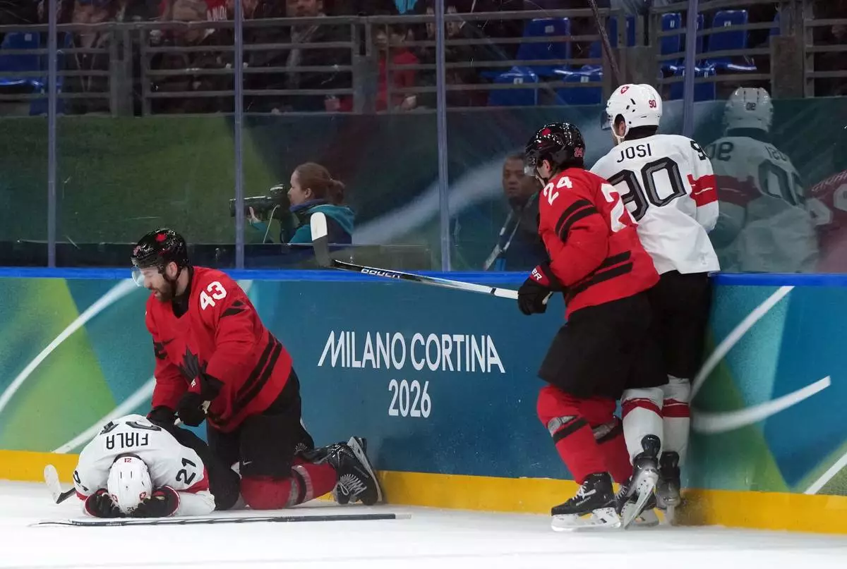 Injured Switzerland's Kevin Fiala lays on the ice after being hit by Canada's Tom Wilson, second left, during a preliminary round match of men's ice hockey between Canada and Switzerland at the 2026 Winter Olympics, in Milan, Italy, Friday, Feb. 13, 2026. (Darryl Dyck/The Canadian Press via AP)