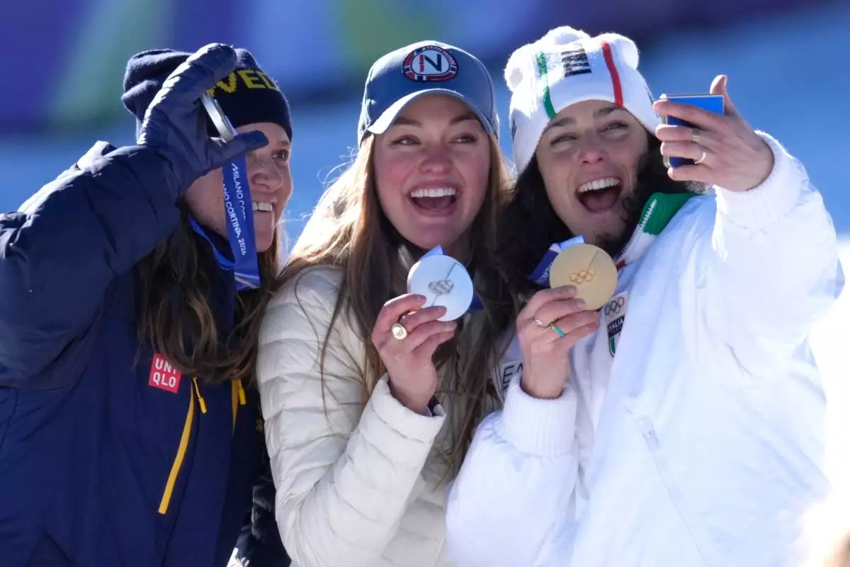 Italy's Federica Brignone, right, celebrates winning gold medal next to joint silver medalists Norway's Thea Louise Stjernesund and Sweden's Sara Hector, left, at the finish area of an alpine ski, women's giant slalom race, at the 2026 Winter Olympics, in Cortina d'Ampezzo, Italy, Sunday, Feb. 15, 2026.. (AP Photo/Robert F. Bukaty)