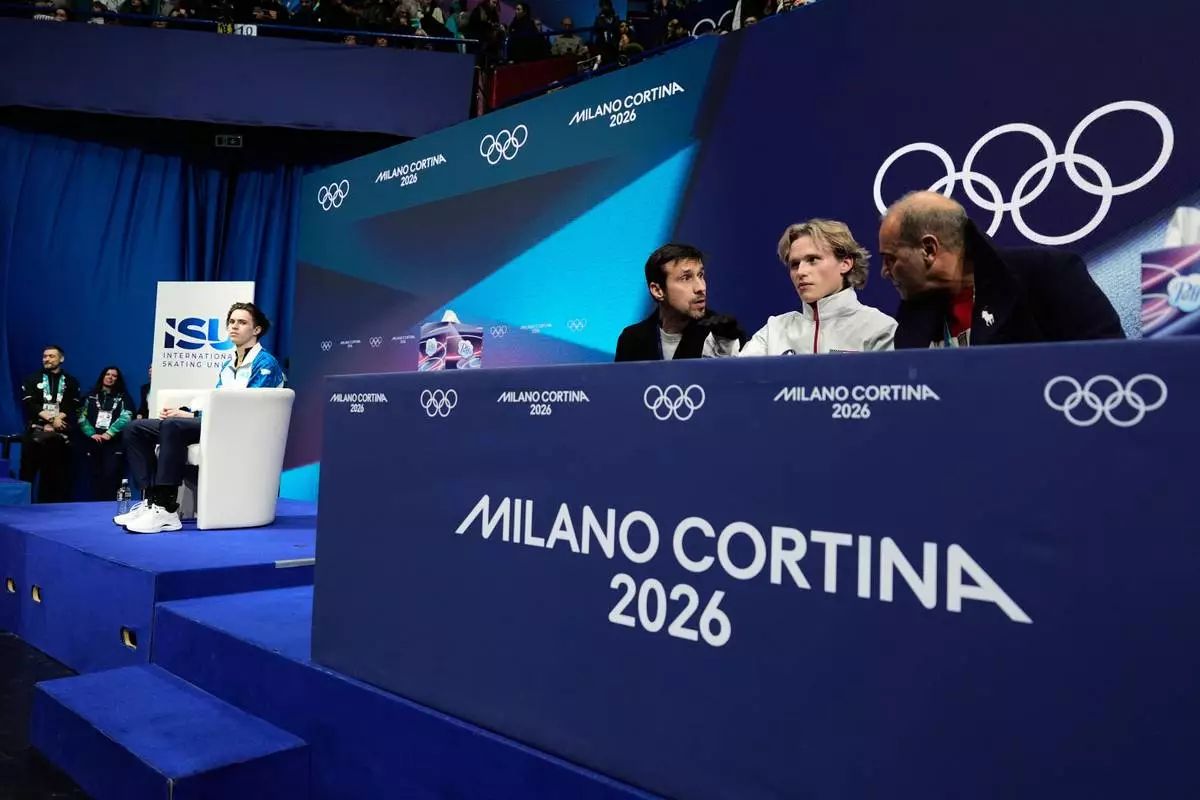 Ilia Malinin of the United States reacts after competing while Mikhail Shaidorov of Kazakhstan is seen on left while waiting for scores during the men's free skate program in figure skating at the 2026 Winter Olympics, in Milan, Italy, Friday, Feb. 13, 2026. (AP Photo/Ashley Landis)