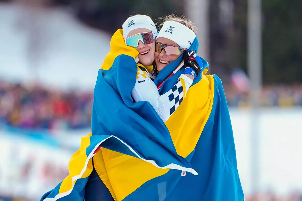 Frida Karlsson, right, and Ebba Andersson, both of Sweden, celebrate after finishing first and second in the cross-country skiing women's 10km + 10km skiathlon at the 2026 Winter Olympics, in Tesero, Italy, Saturday, Feb. 7, 2026. (AP Photo/Matthias Schrader)