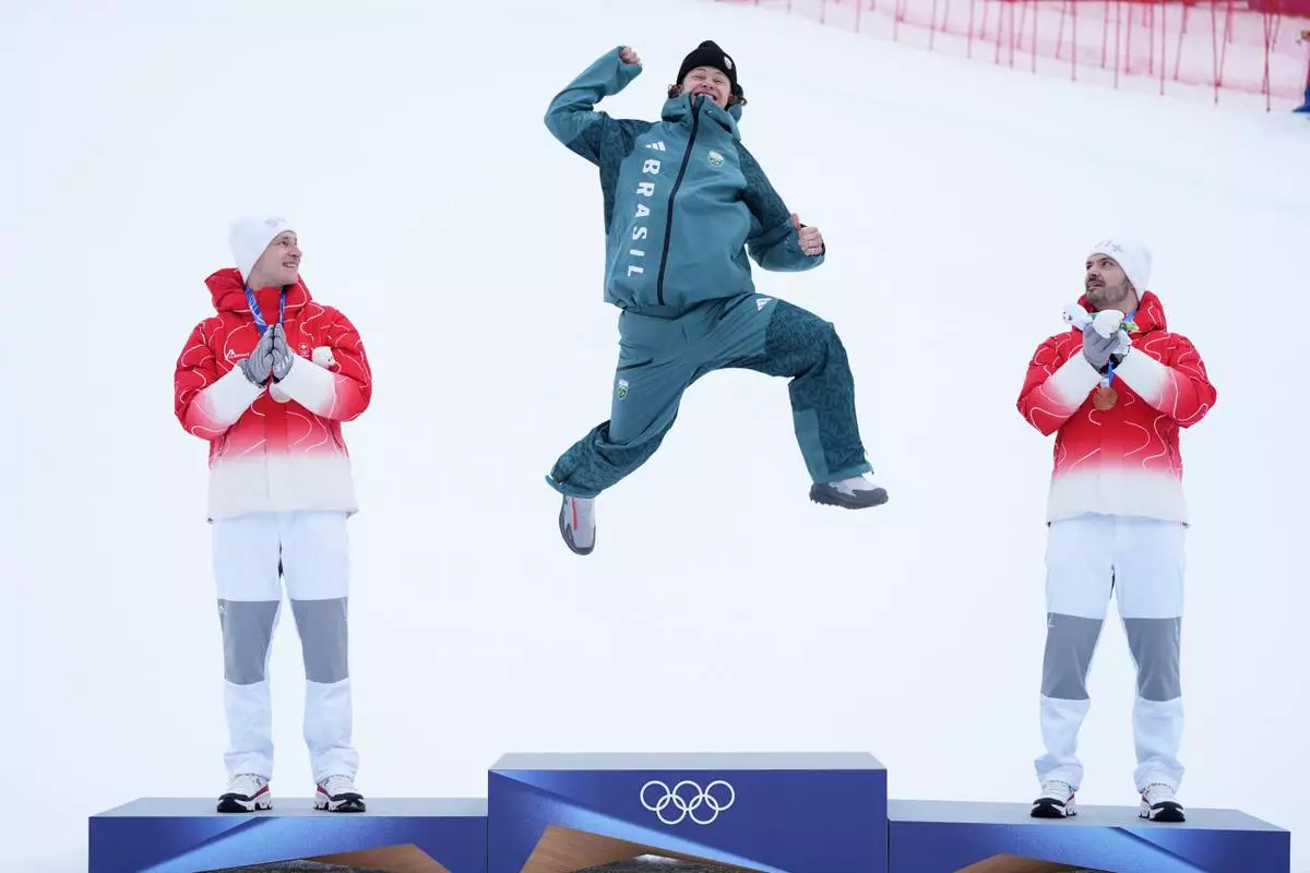 Brazil's Lucas Pinheiro Braathen, center, celebrates winning a gold medal for an alpine ski, men's giant slalom race, as silver medalist Switzerland's Marco Odermatt, right, and bronze medalist Switzerland's Loic Meillard applaud, at the 2026 Winter Olympics, in Bormio, Italy, Saturday, Feb. 14, 2026. (AP Photo/Rebecca Blackwell)