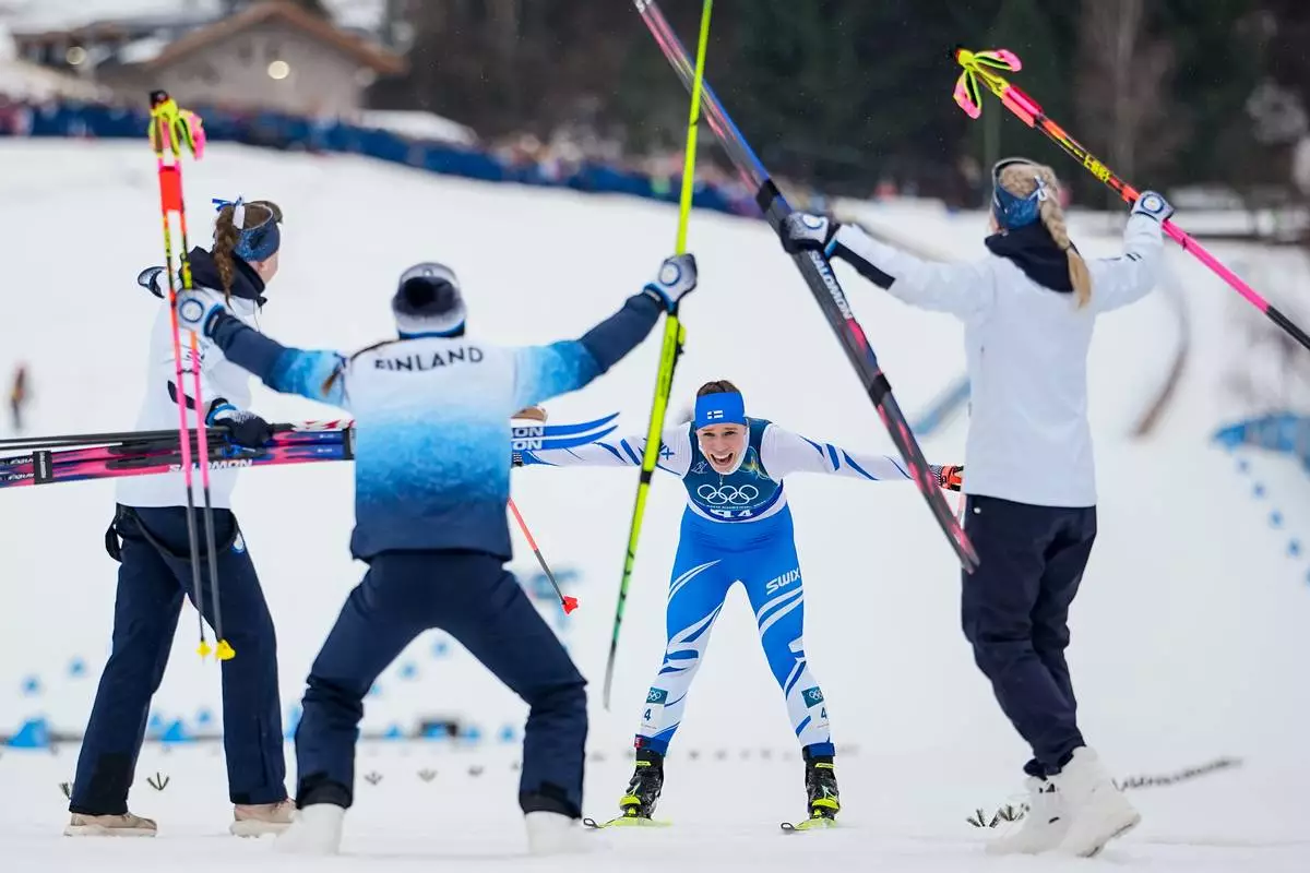 Jasmi Joensuu, of Finland, approaches the finish line and celebrating teammates to win the bronze medal in the cross country skiing women's 4 x 7.5km relay at the 2026 Winter Olympics, in Tesero, Italy, Saturday, Feb. 14, 2026. (AP Photo/Matthias Schrader)