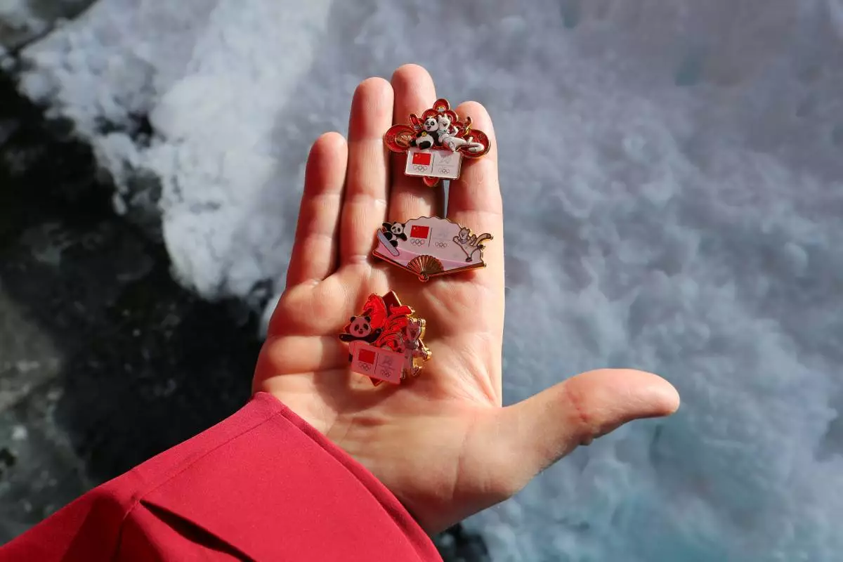 Patrick Shannon, a coach for the Chinese skeleton team, displays China's three pin designs at the Milan Cortina Olympic Village, during the 2026 Winter Olympics, in Cortina d'Ampezzo, Italy, Thursday Feb. 5, 2026. (AP Photo/Jennifer McDermott)