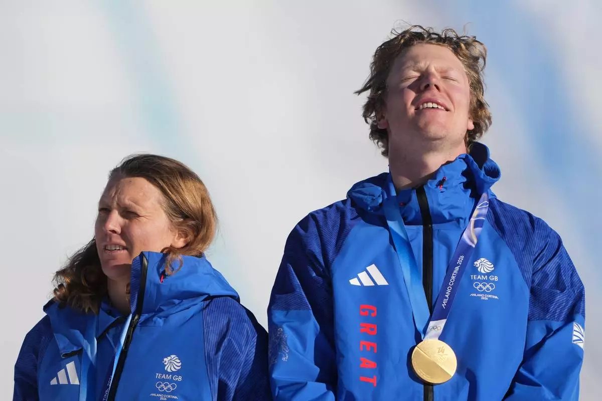 Gold medalists Britain's Charlotte Bankes and Huw Nightingale react on the podium after winning the mixed team snowboard cross finals at the 2026 Winter Olympics, in Livigno, Italy, Sunday, Feb. 15, 2026. (AP Photo/Lindsey Wasson)