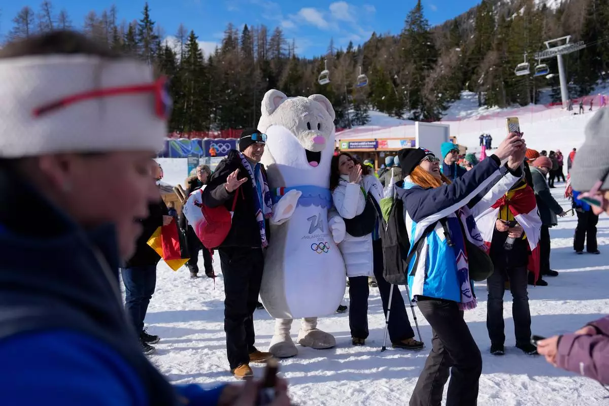 Fans take selfies with the Olympic mascot Tina at the finish area of an alpine ski, downhill portion of a women's team combined race, at the 2026 Winter Olympics, in Cortina d'Ampezzo, Italy, Tuesday, Feb. 10, 2026. (AP Photo/Andy Wong)