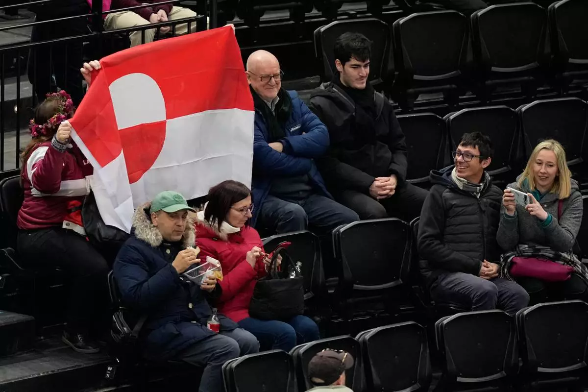 Fans hold Greenland national flag before a preliminary round match of men's ice hockey between United States and Denmark at the 2026 Winter Olympics, in Milan, Italy, Saturday, Feb. 14, 2026. (AP Photo/Hassan Ammar)