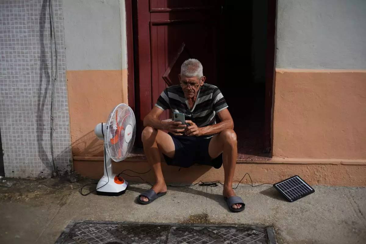 A man charges his phone and his fan with a solar panel during a blackout in Havana, Tuesday, March 17, 2026. (AP Photo/Ramon Espinosa)