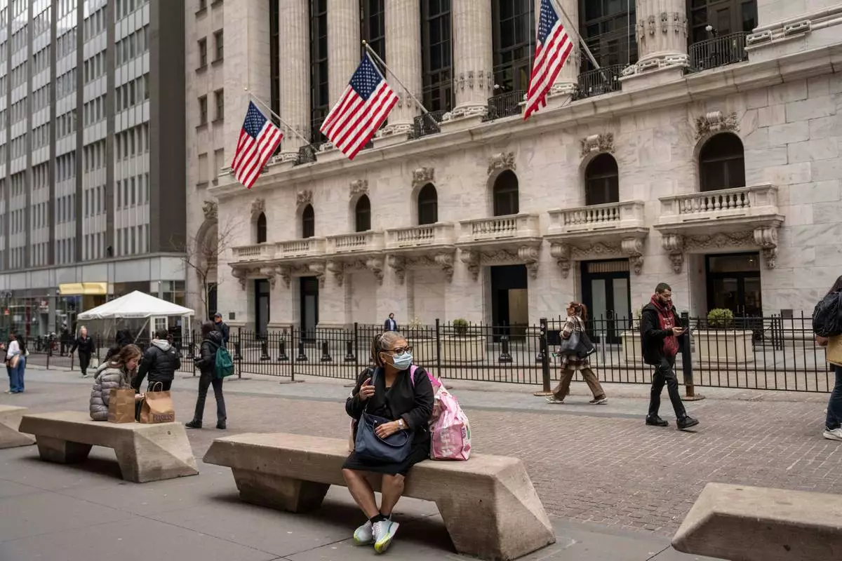 People sit on benches outside the New York Stock Exchange, Friday, March 27, 2026, in New York. (AP Photo/Yuki Iwamura)