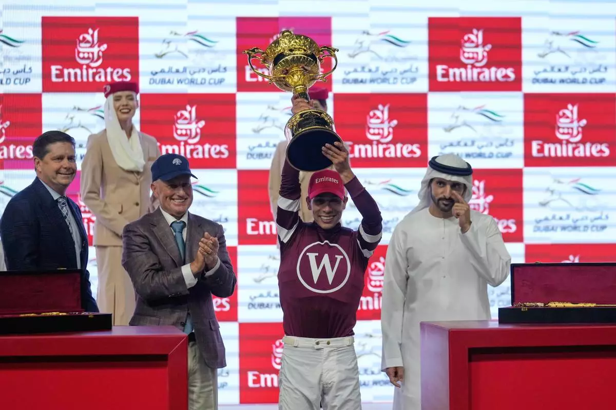 Jockey Jose Ortiz, second right, holds the trophy after riding Magnitude to win the $12 million Dubai World Cup over 2000m (10 furlongs) at Meydan Racecourse in Dubai, the United Arab Emirates, Saturday, March 28, 2026. At left is owner Ron Winchell, and assistant trainer Scott Blasi. (AP Photo/Altaf Qadri)