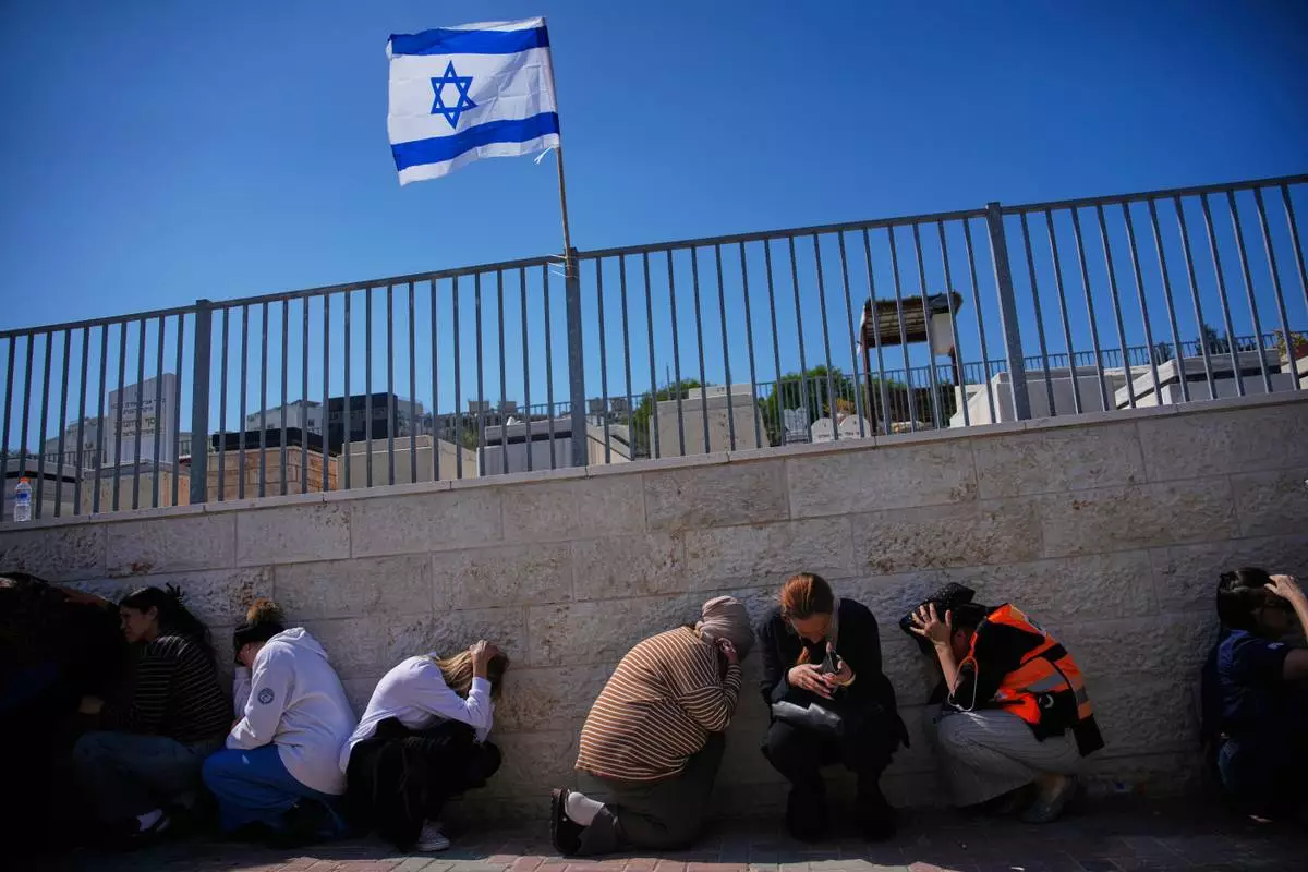 Mourners take cover while air raid sirens warn of incoming missiles launched by Iran toward Israel during the funeral of Sarah Elimelech and her daughter, Ronit, who were killed in an Iranian missile attack, in Beit Shemesh, Israel, Monday, March 2, 2026. (AP Photo/Ohad Zwigenberg)