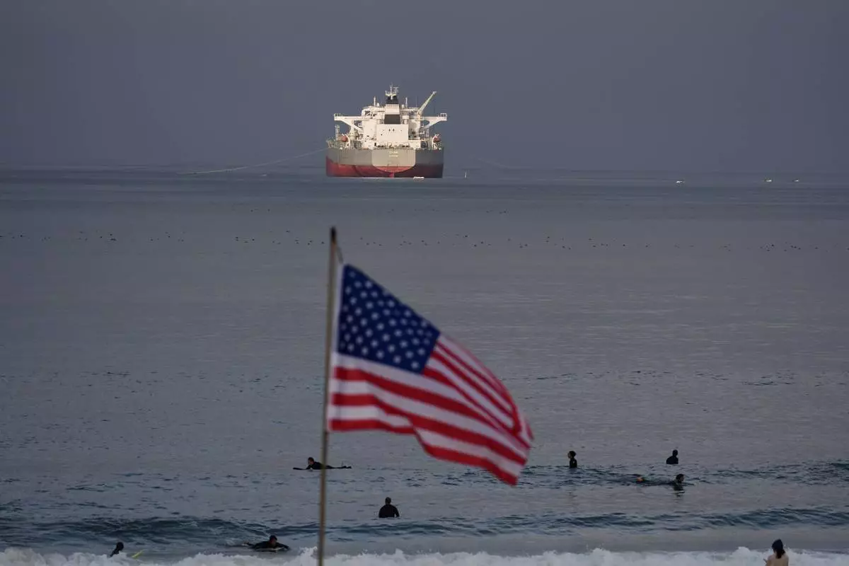 Surfers wait for waves on El Porto Beach as the crude oil tanker "Chios" has its cargo pumped into the Chevron Products Company refinery, one of California's largest petroleum processing facilities, in El Segundo, Calif., on Wednesday, March 4, 2026. (AP Photo/Damian Dovarganes)
