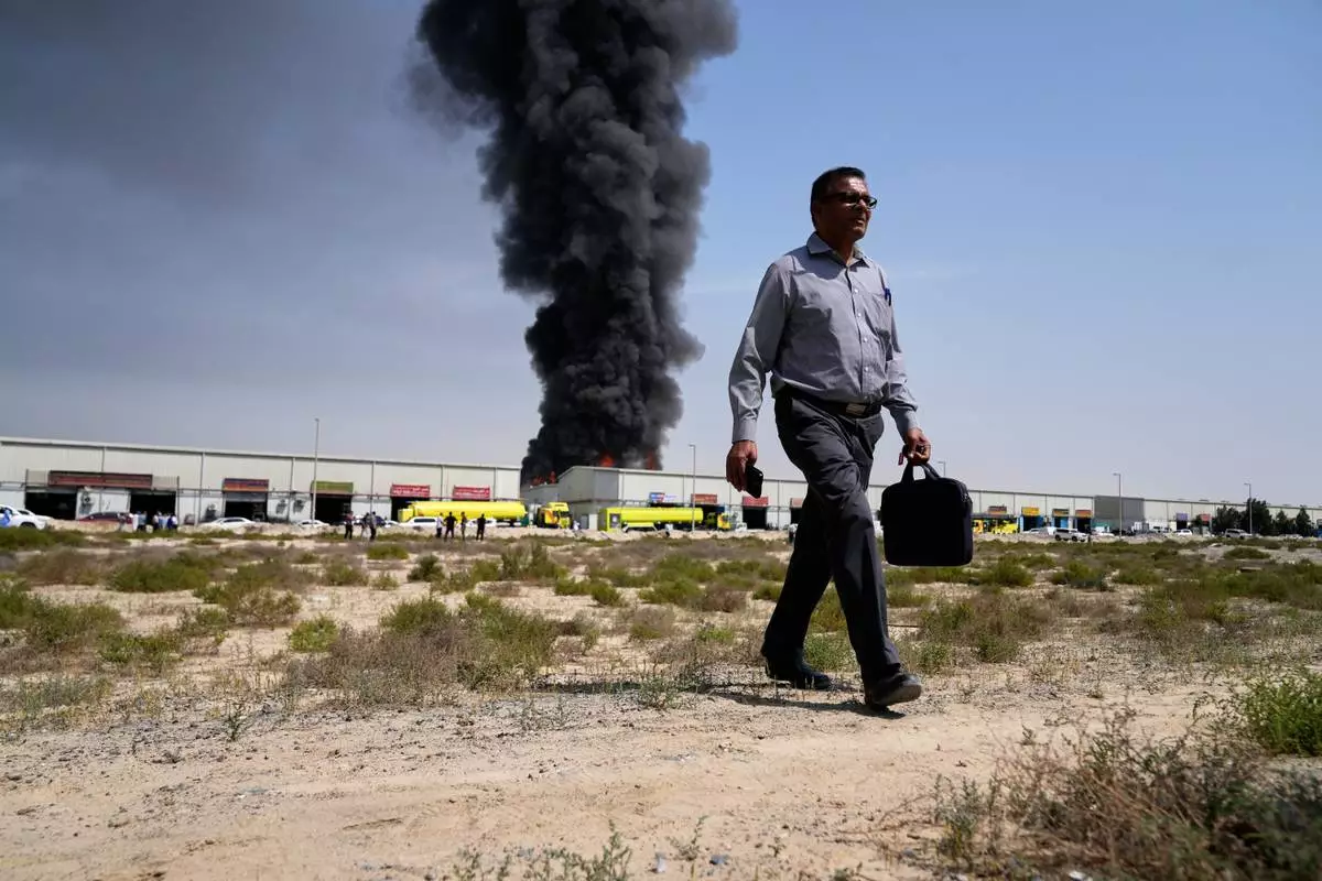 A man walks away after watching a black plume of smoke rising from a warehouse in the industrial area of Sharjah City, United Arab Emirates, Sunday, March 1, 2026, following reports of Iranian strikes in Dubai. (AP Photo/Altaf Qadri)