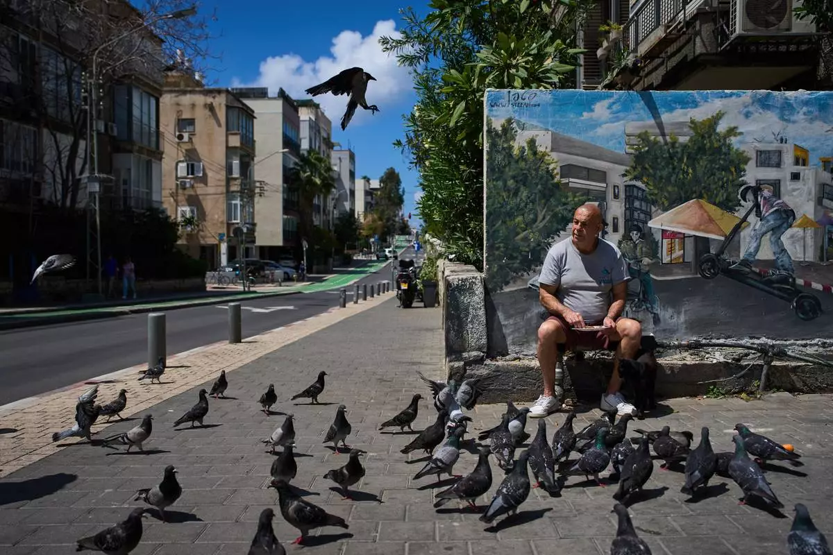 FILE - A man feeds birds on a street in Tel Aviv, Israel, after the announcement of a two-week ceasefire with Iran, Wednesday, April 8, 2026. (AP Photo/Oded Balilty, File)