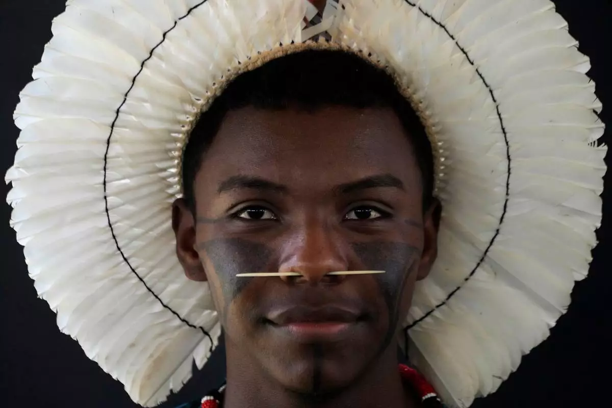 FILE - An Indigenous man wearing traditional face paint, feather headdress and piercing poses for a portrait during the opening of the "Acampamento Terra Livre," or Free Land Encampment, Brazil's largest annual Indigenous mobilization that focuses on land rights and environmental protection, in Brasilia, Brazil, Monday, April 6, 2026. (AP Photo/Eraldo Peres, File)