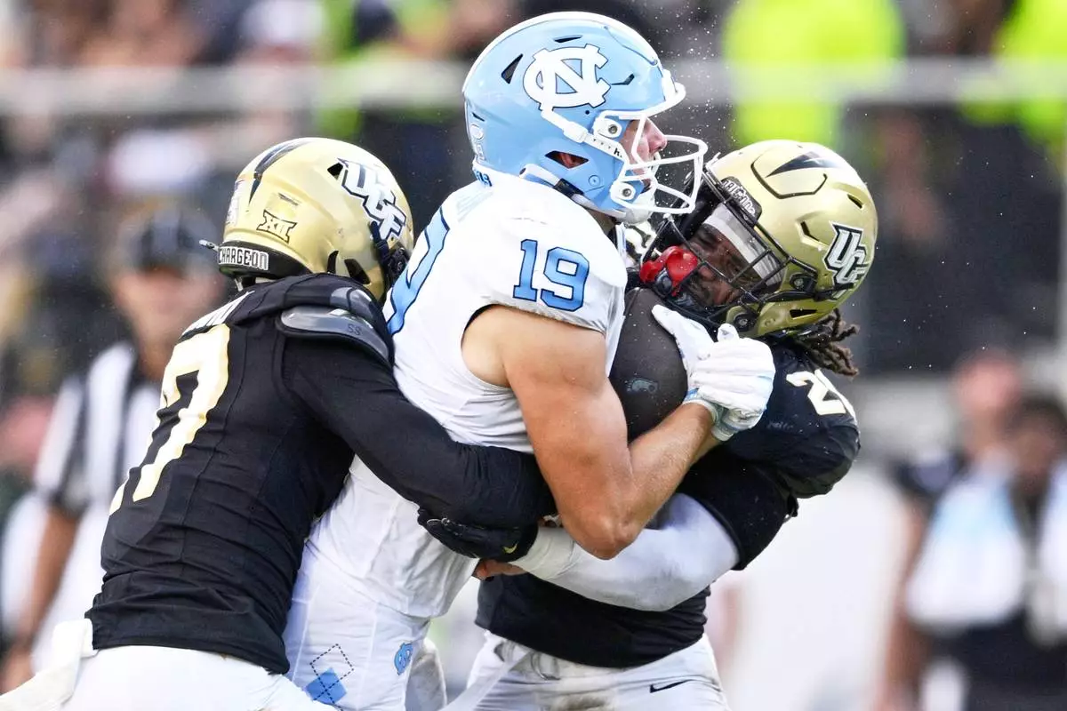 FILE - North Carolina tight end Jake Johnson (19) is tackled by Central Florida defensive back Jaylen Heyward, left, and linebacker Lewis Carter, right, after catching a pass during the second half of an NCAA football game, Sept. 20, 2025, in Orlando, Fla. (AP Photo/Phelan M. Ebenhack, File)