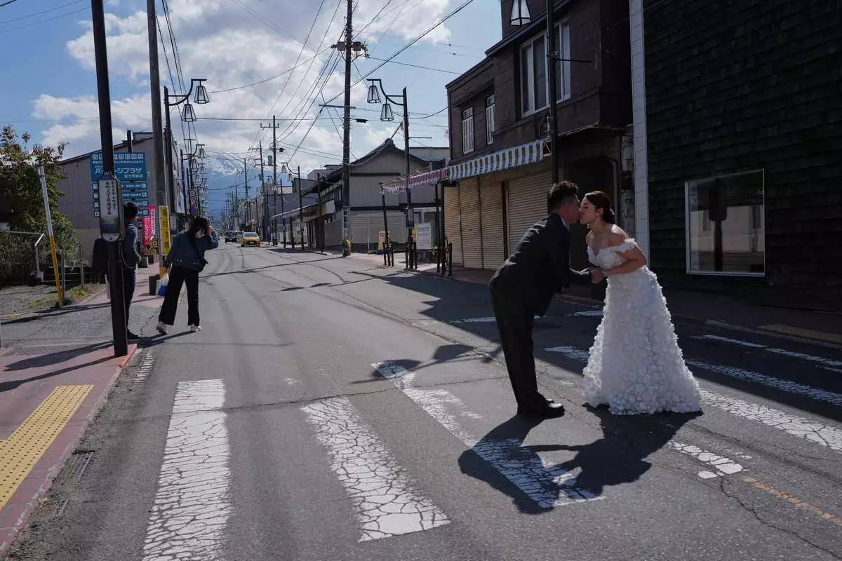 Foreign visitors pose for photos at Honcho Street with Mt. Fuji as background on Wednesday, April 8, 2026, in Fujiyoshida, west of Tokyo. (AP Photo/Eugene Hoshiko)