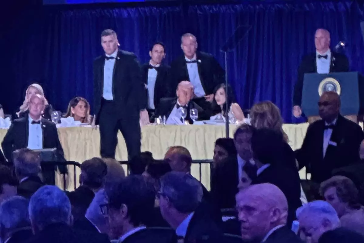 U.S. Secret Service agents surround President Donald Trump before he was taken from the stage after a shooting incident outside the ballroom during the White House Correspondents Dinner, Saturday, April 25, 2026, in Washington. (AP Photo/Alex Brandon)