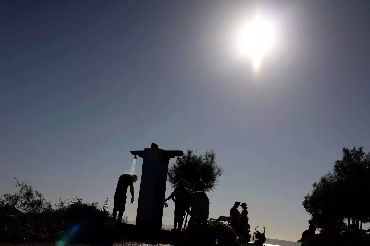 FILE - A man takes a shower near a beach during a hot day in Palaio Faliro suburb, south of Athens, Greece, July 6, 2025. (AP Photo/Yorgos Karahalis, File)