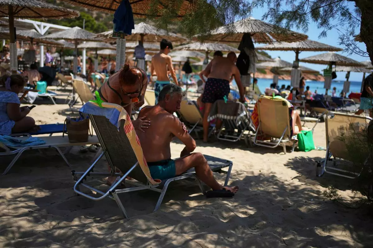 FILE - A woman applies sunscreen to a man at Avlaki beach east of Athens, Greece, Aug. 7, 2025. (AP Photo/Thanassis Stavrakis, File)