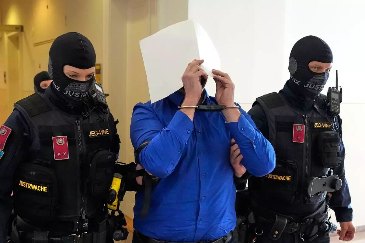 Defendant Beran A. is hiding his face behind file folders when he is escorted out of the courtroom in the District Court in Wiener Neustadt, Austria, where he stands trial for plotting to carry out an attack on one of superstar singer Taylor Swift's concerts in Vienna in August 2024 and pledging allegiance to the Islamic State group, Tuesday, April 28, 2026. (AP Photo/Matthias Schrader)