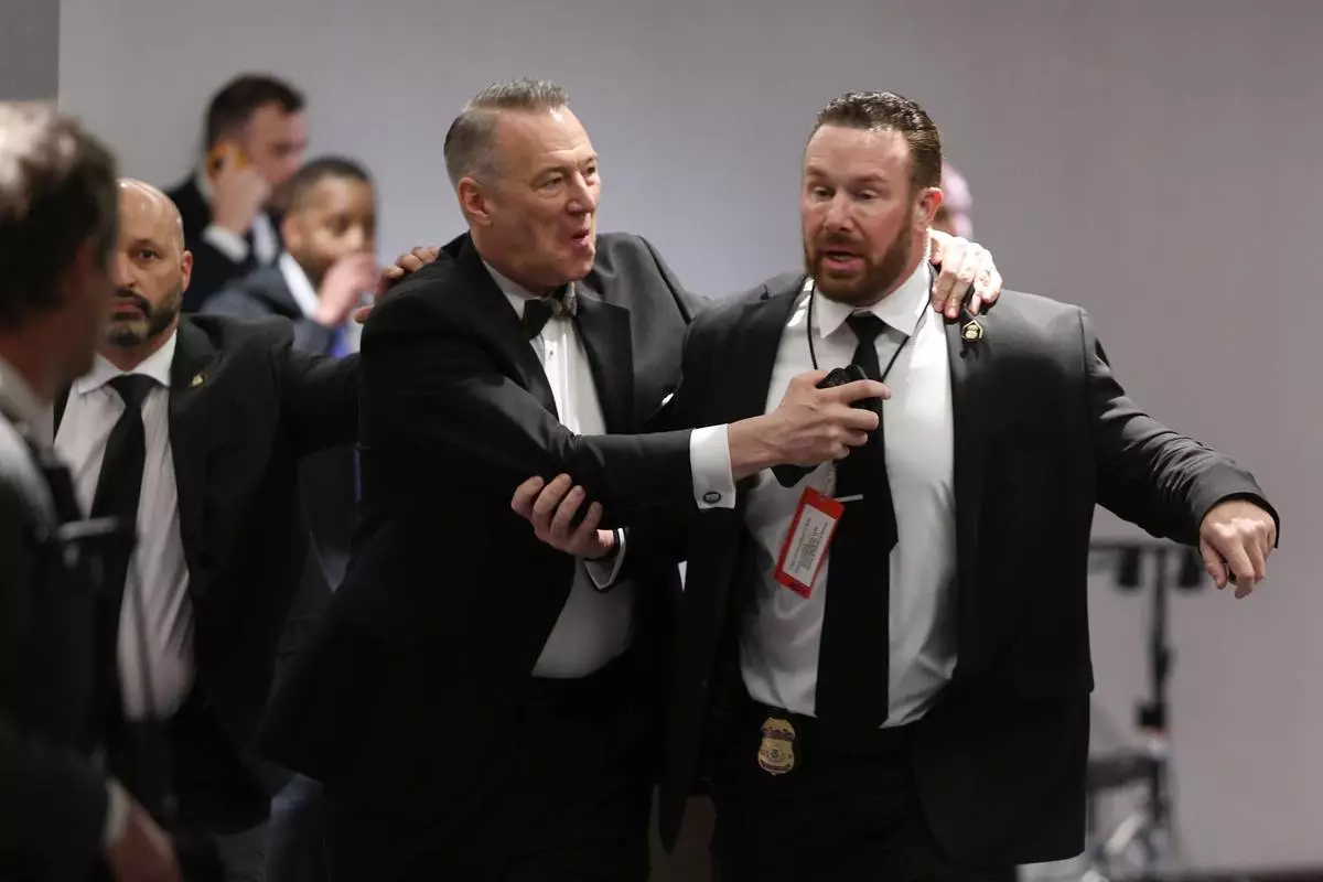 Officers assist guests to exit during the White House Correspondents Dinner, Saturday, April 25, 2026, in Washington. (AP Photo/Tom Brenner)