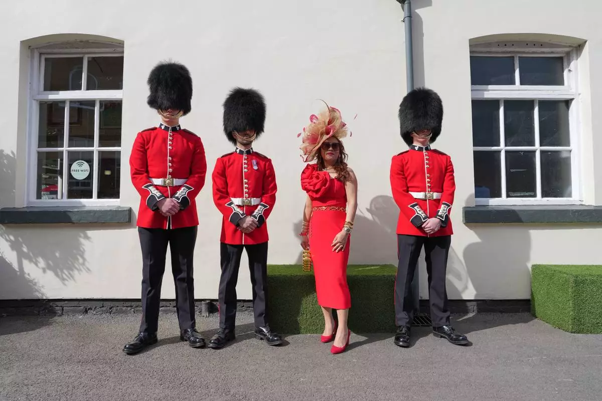 A racegoer poses for a picture with soldiers on Ladies Day, the second day of the Grand National Horse Racing festival, at Aintree racecourse, near Liverpool, England, Friday, April 10, 2026. (AP Photo/Jon Super)