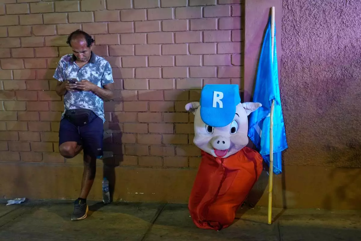 FILE - A supporter of Popular Renewal presidential candidate Rafael López Aliaga, who has embraced the name nickname “Porky”, leans a against a wall alongside his “Porky” costume, in Lima, Peru, March 31, 2026. (AP Photo/Martin Mejia, File)