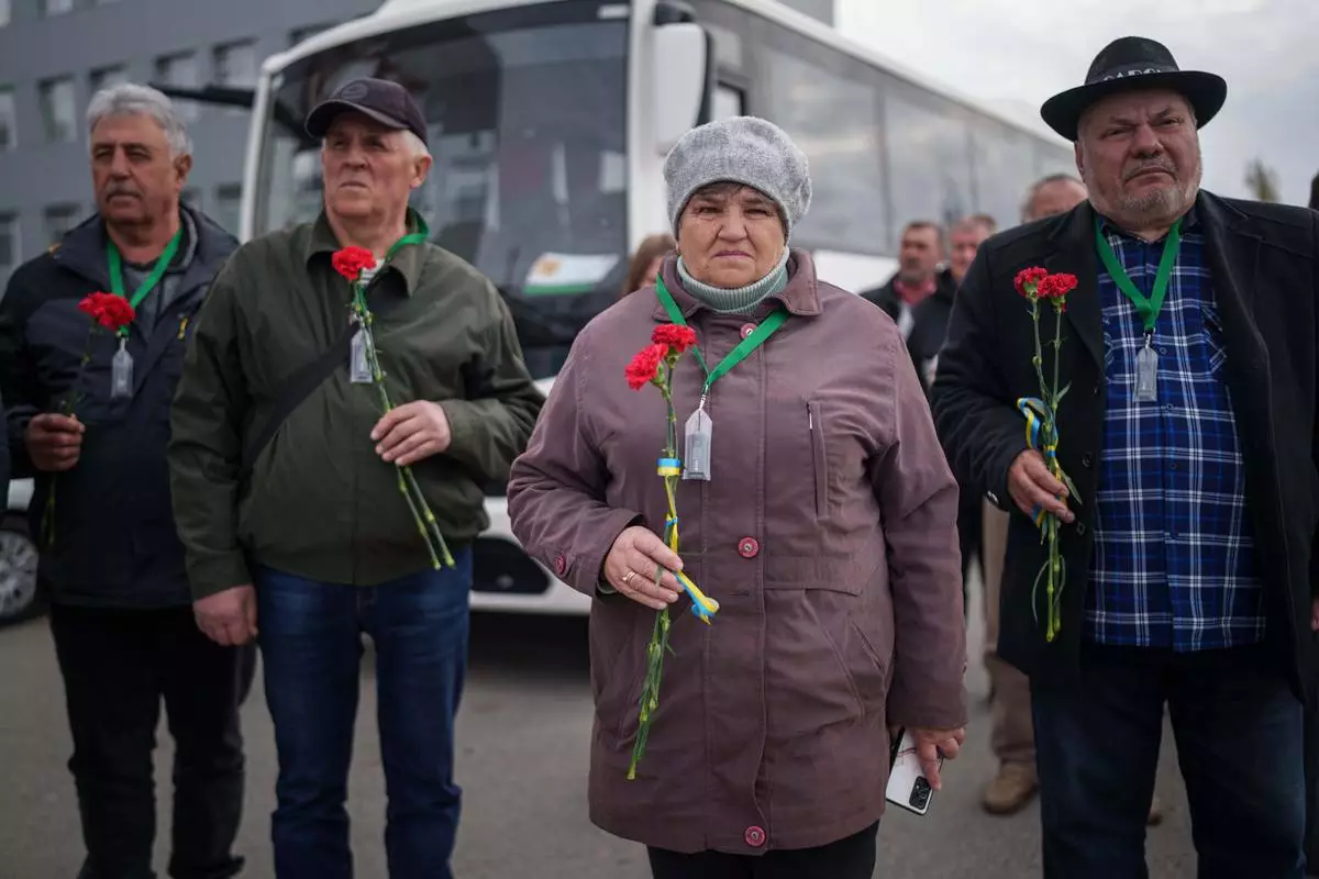 Workers who helped clean up contamination from the Chernobyl nuclear power plant disaster hold flowers before placing them on a monument to their fallen comrades near the plant in Chernobyl, Ukraine, Tuesday, April 21, 2026. (AP Photo/Evgeniy Maloletka)