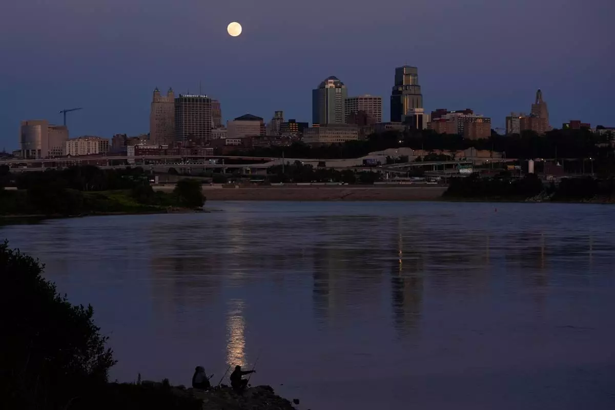 FILE - People fish in the Kansas River as the full moon rises beyond the downtown skyline, May 11, 2025, in Kansas City, Mo. (AP Photo/Charlie Riedel, file)