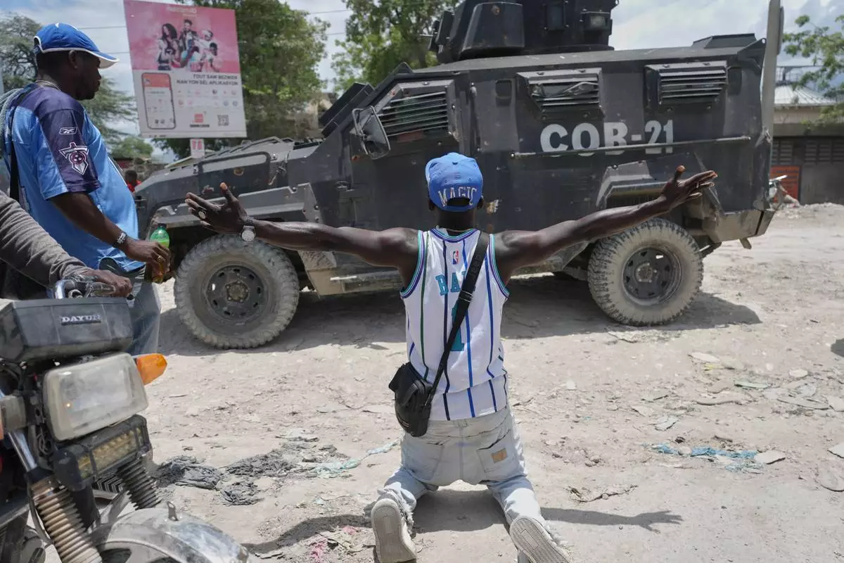 FILE - A resident of Cité Soleil kneels before a police armored vehicle and demands that the police go and fight the gangs that control their neighborhood, in Port-au-Prince, Haiti, May 12, 2026. (AP Photo/Odelyn Joseph, File)