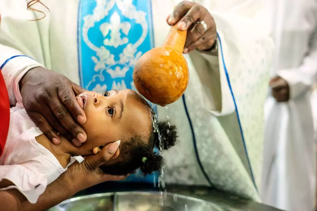 A priest pours water over the head of a child during a baptism ceremony at the Roman Catholic Cathedral in Harare, Zimbabwe, Sunday, April 5, 2026. (AP Photo/Aaron Ufumeli)