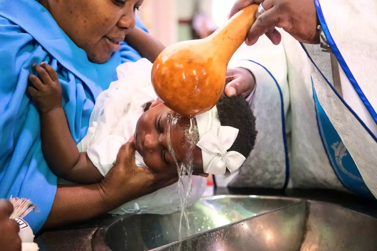 A priest pours water over the head of a child during a baptism ceremony at the Roman Catholic Cathedral in Harare, Zimbabwe, Sunday, April 5, 2026. (AP Photo/Aaron Ufumeli)