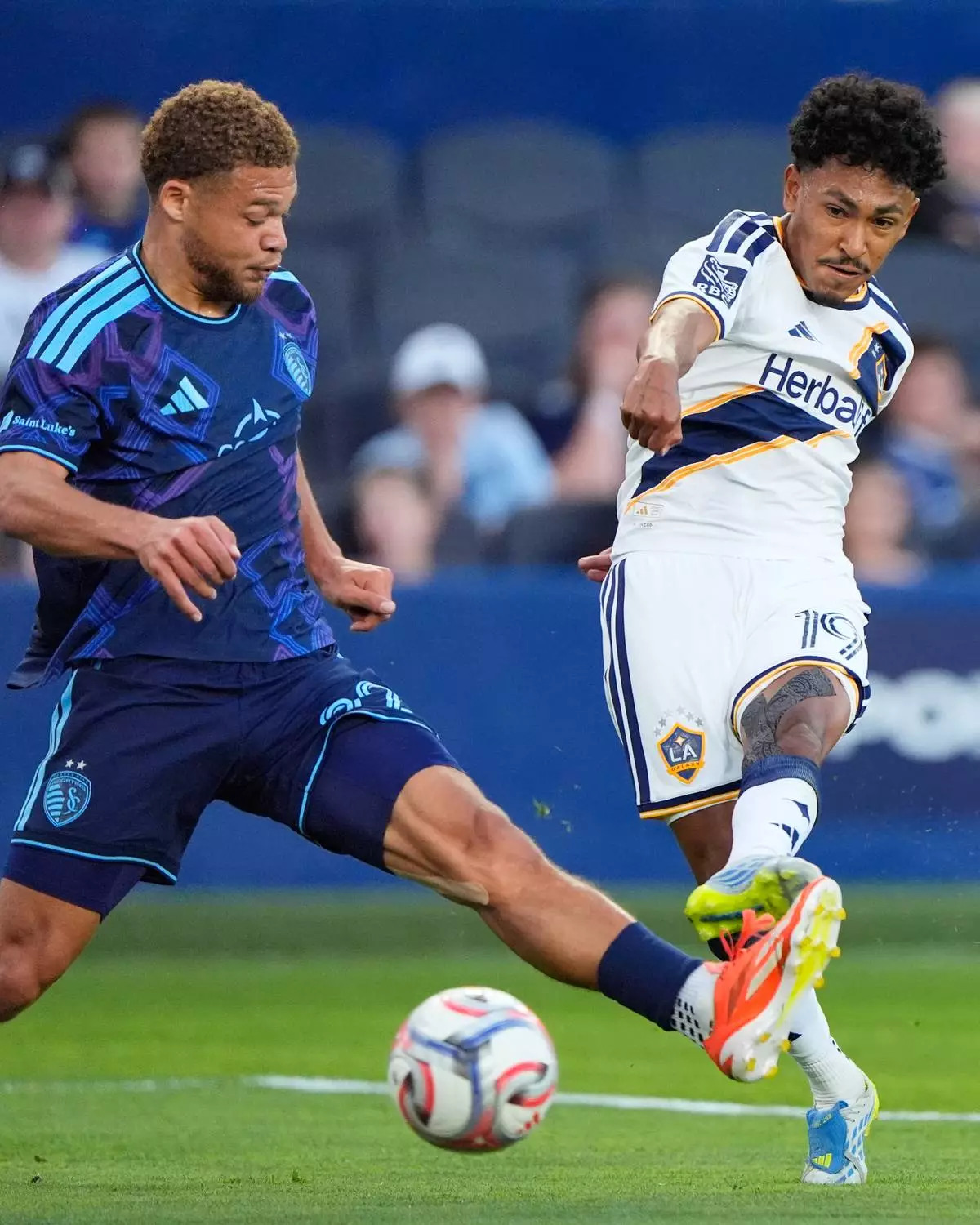 LA Galaxy defender Mauricio Cuevas (19) kicks the ball past Sporting Kansas City midfielder Zorhan Bassong (22) during the first half of an MLS soccer match Wednesday, May 13, 2026, in Kansas City, Kan. (AP Photo/Charlie Riedel)