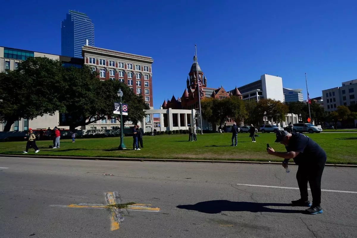 FILE - A person uses a cell phone to take pictures of an X on Elm Street at Dealey Plaza, one of two spots marked where President John F. Kennedy was shot, as people gather on the 60th anniversary of his assassination, Nov. 22, 2023, in Dallas. (AP Photo/Julio Cortez, File)