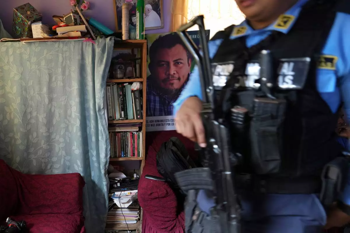 FILE - A poster of slain environmentalist Juan López hangs in his home as a state-assigned bodyguard watches over the López family, in Tocoa, Honduras, Dec. 6, 2024. (AP Photo/Moises Castillo, File)