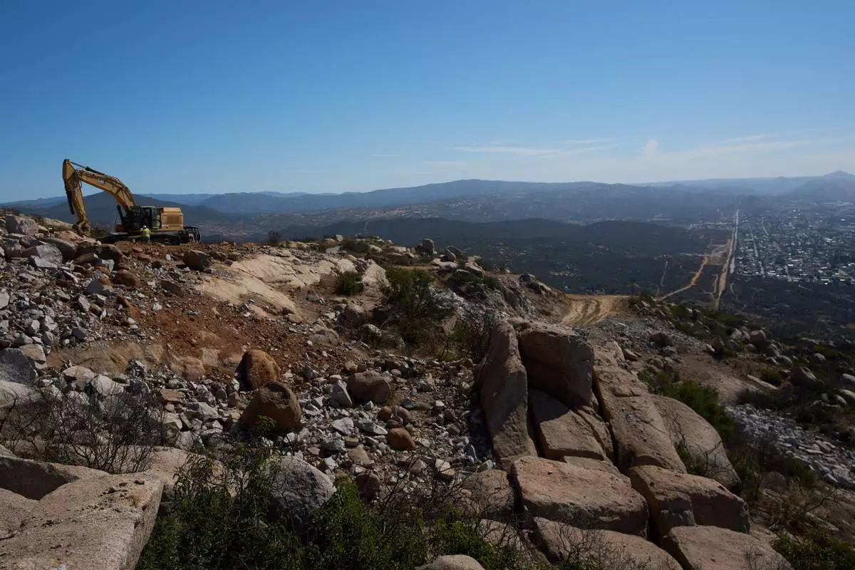 Construction crews work on a new border wall segment on Kuuchamaa Mountain, Friday, April 24, 2026, seen from Tecate, Mexico. (AP Photo/Gregory Bull)