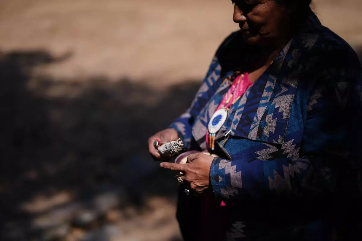 Norma Meza Calles, a Kumeyaay Nation leader, lights a bundle of white sage as she talks of the sacred importance of nearby Kuuchamaa Mountain at a wellness center Friday, May 1, 2026, in Tecate, Mexico. (AP Photo/Gregory Bull)